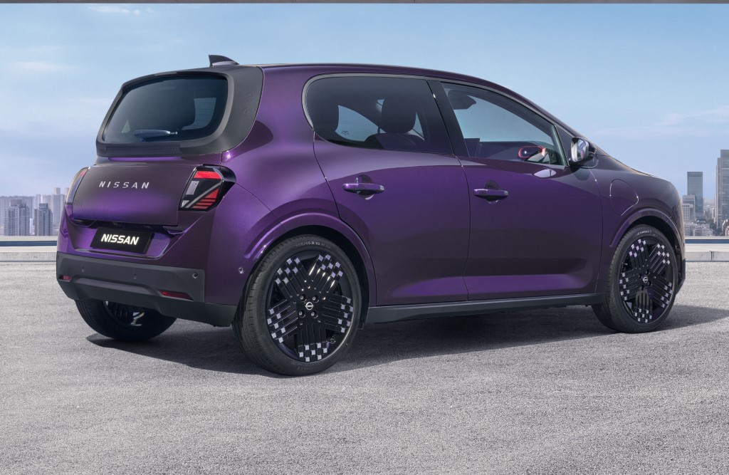 Three-quarter rear view of a purple Nissan PIXO electric city car parked beneath a modern concrete structure, with a city skyline in the background.